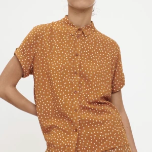 Prickig skjorta från Samsoe Samsoe  - Säljer en kortärmad orange skjorta med vita prickar på från märket Samsoe Samsoe. 100 % viskos. Aldrig använt. Ordinarie pris 799 kr. 