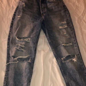 Håliga mom jeans - Blåa mom jeans med hål från H&m i storlek 34. Säljes för 160 kr, gratis frakt