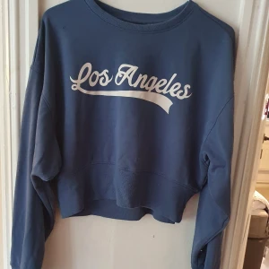 Blå kort sweatshirt - Blå croppad sweatshirt med texten "Los Angeles". Lappen med storleken är borta, men sitter som en oversized S ⭐ Breda ärmar, vilket gör den väldigt bekväm! Bra skick men välanvänd. Säljs då den ej används. Kontakta vid frågor/intresse 💜 frakt inräknad