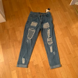 Oanvända jeans-storlek 38. - Boyfriendjeans från boohoo. Helt oanvända och i storlek 38. Mörkare jenasfärgade men hål på framsidan. Nypris 400kr mitt pris 100kr + frakt eller mötas.