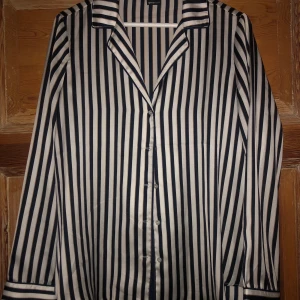 Randig skjorta  - En fin randig skjorta med vit botten och ränder i marinblått och beige/brun. Sidenmaterial och väldigt bra passform! Köparen står för frakten och det angivna fraktpriset kan ändras! 