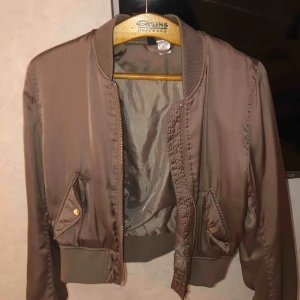  - En tunn bomberjacka i gott skick, samt nästan helt oanvänd. Mörkbeige färg och guldiga kedjor och knapp. Pris 150 kr + fraktkostnader😊😊