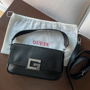 GUESS handväska - svart - FLYTTRENS!! Guess handväska i svart skin, som ny - kommer med axelband och crossbody i orginal dustbag