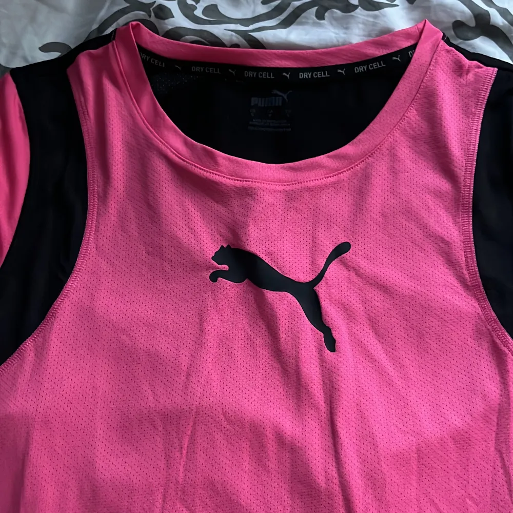 En rosa och svart t-shirt från Puma med korta ärmar. T-shirten har en svart Puma-logga på bröstet och är tillverkad i ett andningsbart material.. T-shirts.