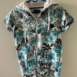 Kortärmad Huvtröja - Kortärmad huvtröja med delad känguruficka och full-längds dragkedja. Broderi se bild. Kapushong med dragsko. St. M Bomull  I fint använt skick.