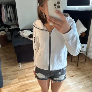 Vit jacka med dragkedja - En vit hoodie från Pelle P med dragkedja framtill. Jackan har en huva och två fickor på framsidan. Märkets logotyp finns på vänster ärm.