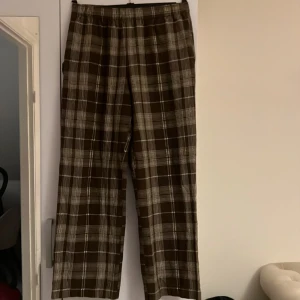 Bruna rutiga byxor  - Fickor. En ficka också på benet och ett litet band vid fickan på sidan. Resår runt hela midjan 