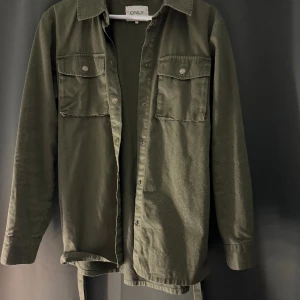 Grön jacka från only  - Grön jacka från only. Något längre i modellen med band som kan knytas runt midjan. Säljs då den inte kommer till användning längre