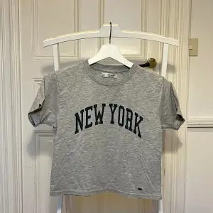 Grå kort tshirt från Pull&Bear med ”NEW YORK” tryckt på framsidan i marinblått. Använd sparsamt men inga defekter.