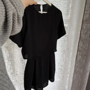 Svart jumpsuit - Jättesöt jumpsuit/byxdress från New Look. Dragkedja i ryggen, fint fall. Som en liten klänning med ben 💓Sparsamt använd och i fint skick 💕