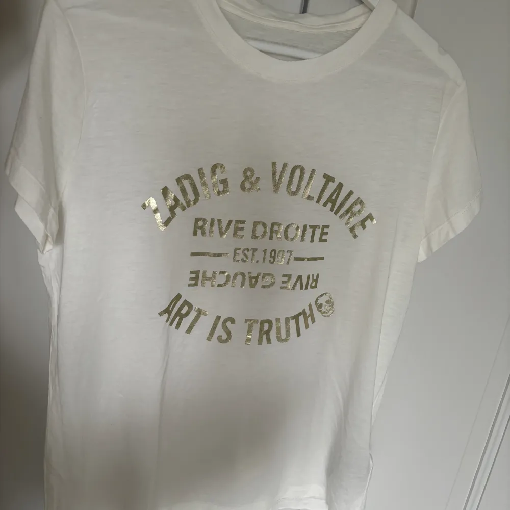 Säljer supersnygg vit t-shirt med guld tryck i strl S som tyvärr inte har kommit till användning🩷Nyskick endast använd en gång💗. T-shirts.