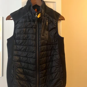 Parajumpers väst blå zavier boy - Mörkblå vadderad väst från Parajumpers. Vadderingen består av polyester. Två fickor framtill samt en med dragkedja. Normal passform storlek YS.  Väldigt liten reva framtill annars i fint skick. Ordinarie pris 2899 SEK 