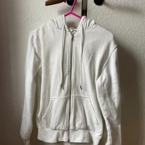 Kofta - En vit zipup hoodie. Metall delarna på snörerna är lite gula och den ena kan gå av. 