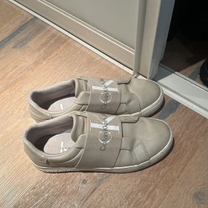 Calvin Klein sneakers - Ett par beiga Calvin Klein sneakers som är nästan helt i nyskick förutom under skon där man ser att de är lite annvända. Storlek 37 men de är stora i storlek så passar 38 också!😊