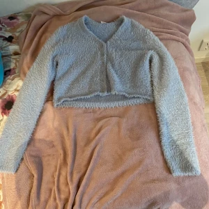 Grå fluffig croppad kofta - Säljer en supermysig ljus blå fluffig kofta. Den har långa ärmar. Perfekt för höst och vinter när man vill vara både varm och stilren. Koftan är i mycket bra skick och passar perfekt till både vardag och fest. 🩶