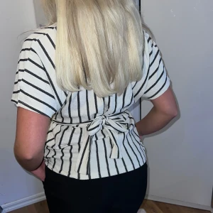 Randig omlottopp med knytband - Säljer en superfin randig omlottopp i vitt och svart. Toppen har korta ärmar och ett knytband i midjan som ger en snygg passform. Perfekt för både vardag och fest!