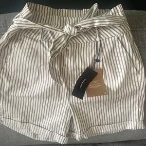 Paperbag shorts   - Söta paperbag shorts med vit/beige randigt mönster, från Vero Moda. Oanvända med lapparna kvar, nypris 350 kr. Storlek small. Hör gärna av dig vid frågor!