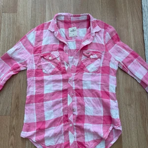 Rutig skjorta från Hollister - En rutig skjorta från Hollister i rosa och vit färg🤗Skjortan har långa ärmar och två bröstfickor med knappar. storlek xs