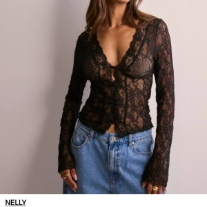 Svart spetsblus från Nelly - Säljer en superfin svart spetsblus från Nelly. Den är genomskinlig och har en v-ringad design med knappar framtill. Blusen är långärmad och har en tight passform, perfekt för festliga tillfällen. Materialet är mjukt och stretchigt, vilket gör den bekväm att bära.