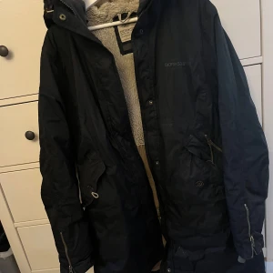 Svart jacka från Didriksons - En svart jacka från Didriksons med dragkedja och knappar. Jackan har en huva och är fodrad med ett mjukt material. Den har flera fickor och justerbara detaljer.