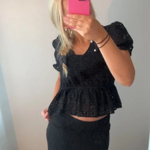 Svart blus med spetsdetaljer - Säljer en superfin svart blus med spetsdetaljer. Den har korta puffärmar och en v-ringad hals. Blusen är croppad och har en volangkant nedtill. Perfekt för både vardag och fest!
