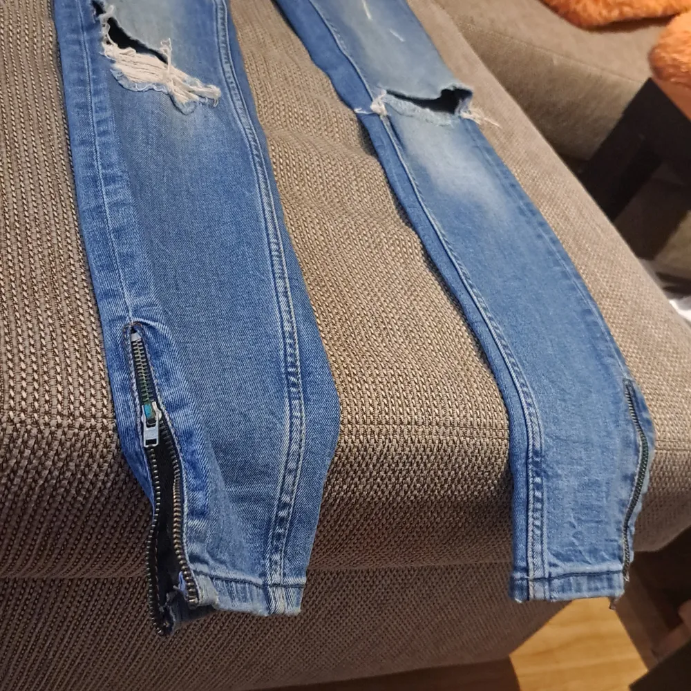 Säljer ett par blå jeans med slitningar och dragkedjor vid bensluten. Jeansen har en tight passform och är i en klassisk blå färg. Perfekta för en avslappnad och trendig look! knappt använd. passar Xs oxh S. Jeans & Byxor.