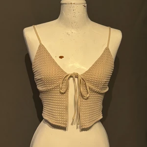 Beige ribbad linnetopp från Divided - Säljer en superfin beige ribbad linnetopp från Divided. Den har smala axelband och en söt knytning framtill. Perfekt för sommaren och kan stylas med både jeans och kjol. Toppen är i storlek XS och är i nyskick. Passar perfekt för både vardag och fest!