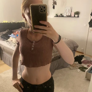 Brun ribbad croppad topp - Säljer en snygg brun ribbad croppad topp. Den har korta ärmar och knappar framtill. Perfekt för en avslappnad sommarlook eller en festkväll. Toppen är i bra skick och väldigt bekväm att ha på sig.
