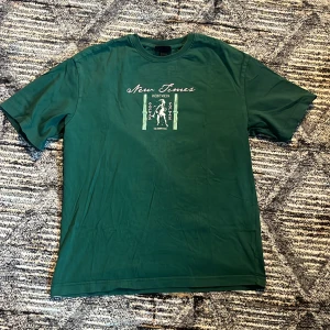 Grön HM tischa - En väldigt skön och fläckfri grön tischa i bomull från H&M i fina färger och fina motiv inspirerat av antika Grekland. Den är i storlek S, men den är också relaxed fit och går att stylea på olika sätt.