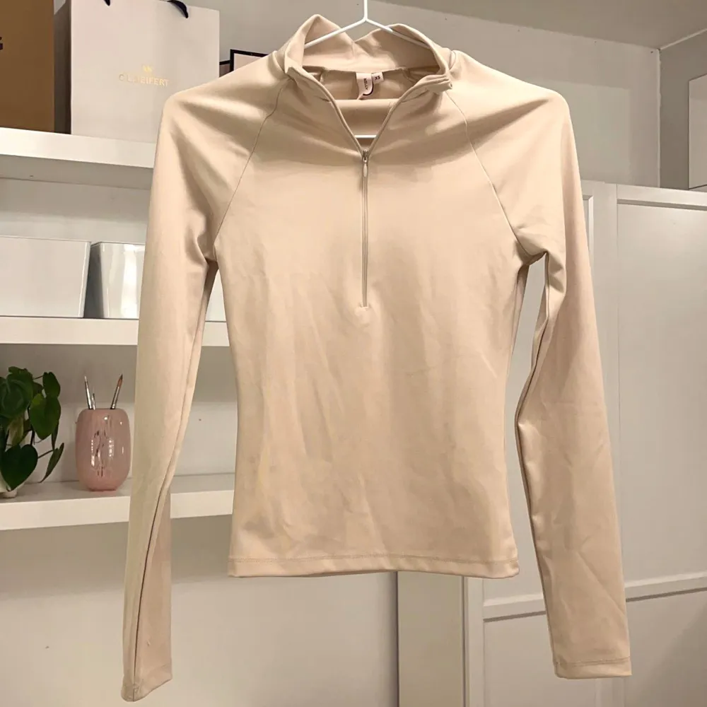 Träningströja från Nelly. Beige färgad. Den har en halv zip (dragkedja) i bysten och är hel täckande i ryggen. Den är aldrig använd och i nyskick, endast provad. Inga fickor. Storlek XS. 💗. Tröjor & Koftor.