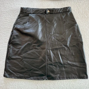 Svart Skinnkjol - Svart skinnkjol från Nelly. Kjolen är inte skrynklig på, utan bara för den legat i en låda under längre tid. Men om man låter den hänga lite blir den som ny 😊.  Använd 1 gång 💥.