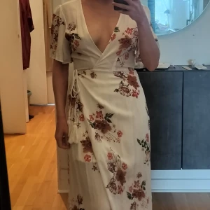 Vit sommarklänning omlottklänning - Fint krinklat material, omlottklänning med somrigt blommigt mönster. Korta ärmar. Använd vid ett tillfälle.