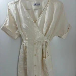 Zara klänning  - Jätte fin beige klänning från Zara i storlek 152-158, man kan ha knuten på båda sidor,  skriv gärna om ni vill ha bild på hur den sitter på! 