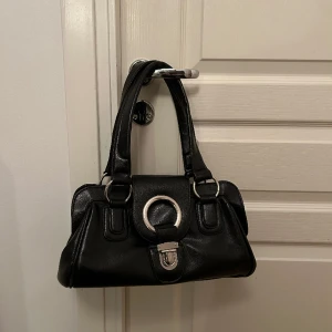 Väska - Svart skinnväska med fina detaljer. Enda defekten är att metallen sticker upp lite på ena sidan. 