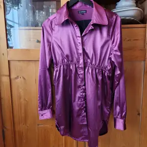En skjortklänning/tunika i en fin lila färg med knappstängning och knappar i ärmsluten och lite slits i sidorna. Storlek 36/38