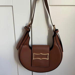 Handväska i brunt konstläder - En brun handväska med gulddetaljer.