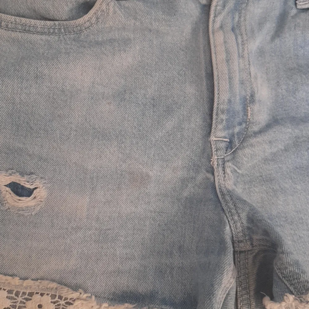 Ett par jätte söta jeans shorts med blommig spets kant ner till och går att dra åt i midjan om man inte vill ha ett skärp. Tyvärr så har den en liten fläk som man ser på sista bilden.. Shorts.