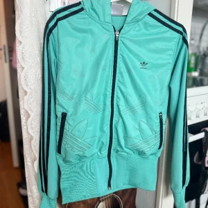 Adidas-jacka - Turkos Adidas-jacka märkt storlek XXL, men sitter bra på mig som är S/M, uppskattar till M. Hel och ren men trycket på framsidan är lite slitet (se bild). Frakt tillkommer. 