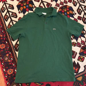 Grön Lacoste Piké  - Hej säljer min gröna snygga Lacoste piké eftersom den blivit för liten. Det är en perfekt kortarmad piké nu inför sommaren. Den är i jätte  bra skick och köpt för nypris 749kr