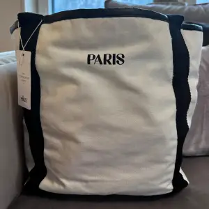 Säljer en väldigt fin ny tygväska med texten: PARIS. Storlek: 30 cm x 30 cm Aldrig använd. Köpt från ELLOS. Perfekt till sommaren / våren och till stranden. 