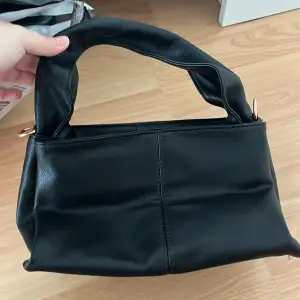 En svart handväska som aldrig är använd. Tillhörande band medföljs.