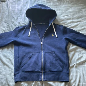 Polo Ralph Lauren zip hoodie - Säljer min nästan oanvända polo zip, den är i 9/10 skick och jag köpte den av min kompis som inte använde den. Den är använd fåtal gånger och jag köpte den för en månad sedan. Den är i Storlek S men lite mindre i storlek. Ny priset var ungefär 1400kr