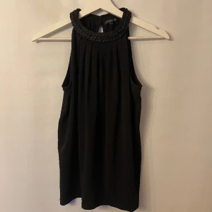 Topp med glittrig halsringning - Svart Topp med glittrig halsringning. Märke: Stockholm. Storlek: Xs men passar även S