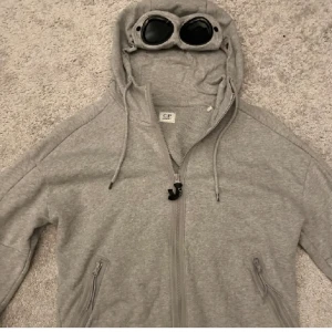 C.P company zip hoodie grå ÄKTA - Säljs för den inte används längre. I väldigt fint skick förutom ett litet ”jack” som inte ens syns, kan skicka bild. Hoodien är äkta och nypris ligger på 3700kr, clg koden skickas. Storlek M, längd 65cm och bredd 45cm. Hör av er vid funderingar 