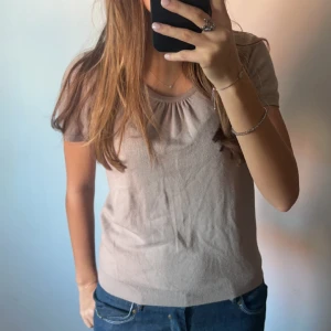 Stickad t-shirt - Säljer denna finstickade t-shirt med scrunsh i fram vid kragen. Säljer då den inte kommer till användning. Lite svårt att säga vilken färg den är, men typ grå/brun. Strl M, men sitter mer som en S💕