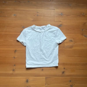 kort topp - Kort t-shirt i kritvit färg, mjuk i materialet och tajt om bysten! Kort i längden och mer crop-top aktig. 