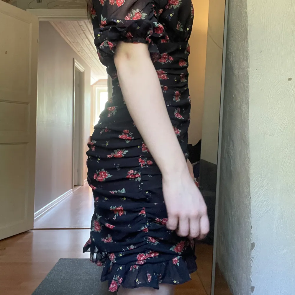 Svart klänning med röda blommor och volanger i ärmarna och längst ner. På mig som är 160cm lång sitter den precis över knäna.. Klänningar.