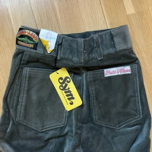 Puss & Kram vintage utsvängda byxor - Äkta vintage byxor, utsvängda svarta/mörkgrå. Från ikoniska svenska märket Puss & Kram. Helt nya med lapp kvar, endast legat på lager. Obs det är rålängd, de är alltså inte fållade utan bör sys upp i ens egen längd. Mått: midja: 29 höft: 35,5 ben: 84