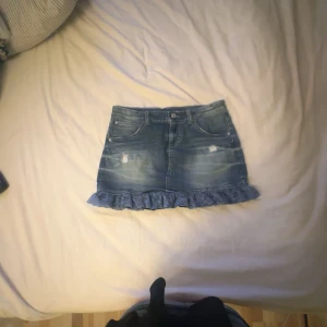 Kort jeans kjol - Säljer denna gulliga jeanskjol med en liten spetsvolang nedtill❣️Kjolen har inga täcken på slitage och är i ett fint skick! Den har som ett inre resårband i midjan, som gör att du lätt kan justera storleken❤️ obs att kjolen har små paljetter  ( bild 4)