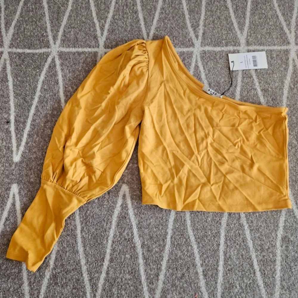 Jättefin croppad one shoulder topp med puffärm. Färgen är senapsgul. Aldrig använd men lite skrynklig då den legat i lådan. Kommer från ett djur och rökfritt hem.. Yläosat.